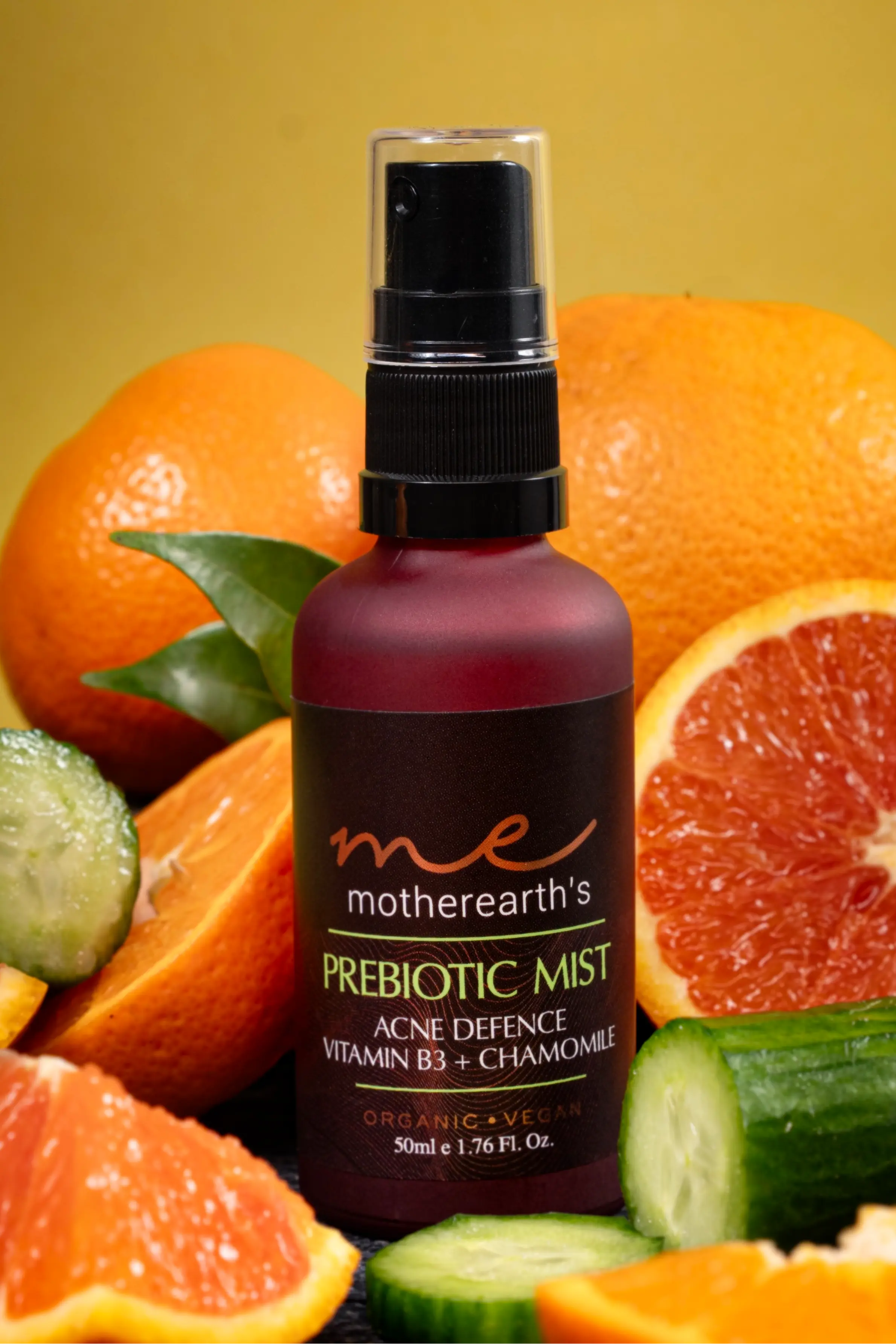 A bottle of prebiotic mist with its ingredients surrounding it: oranges and cucumbers in the background. 